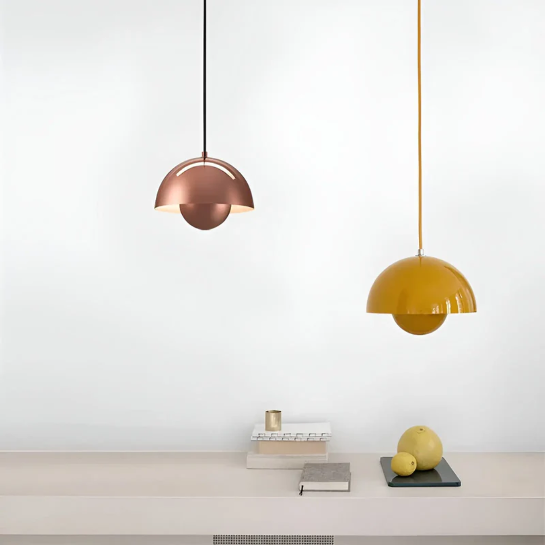 Zwei moderne Pendelleuchten, kupfer und gelb, über minimalistischem Tisch mit Büchern und Früchten.