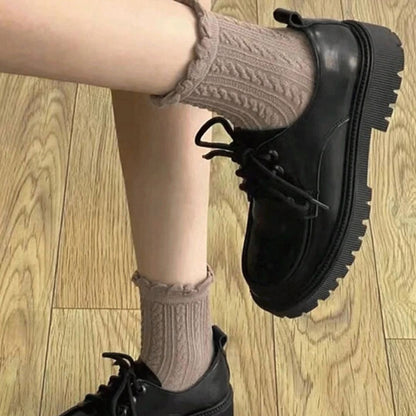 Schwarze Lederschuhe mit dicker Sohle und beige Socken auf Holzboden.