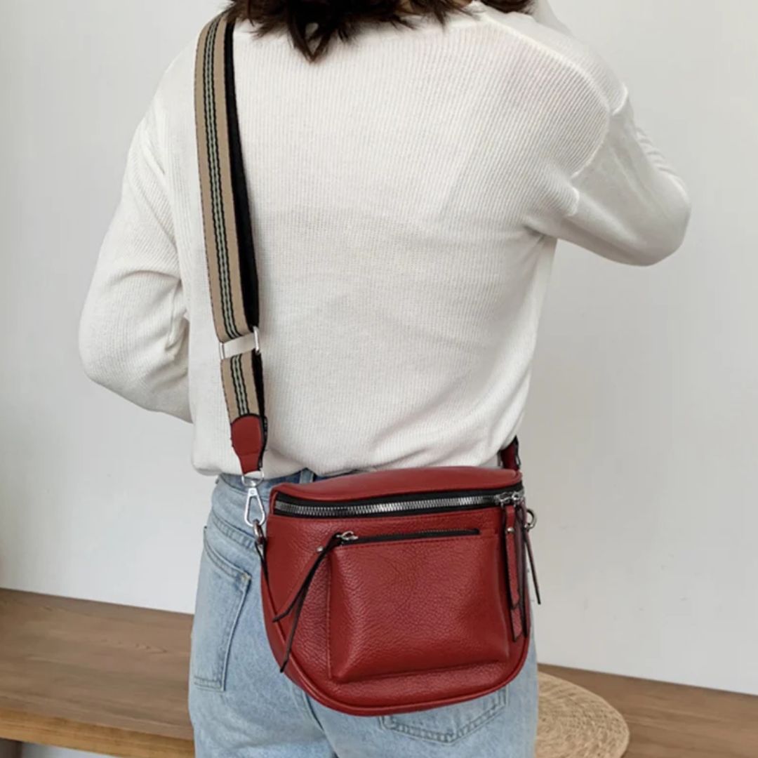Frau mit roter Leder-Umhängetasche, gestreiftem Gurt, weißem Pullover, blauer Jeans.
