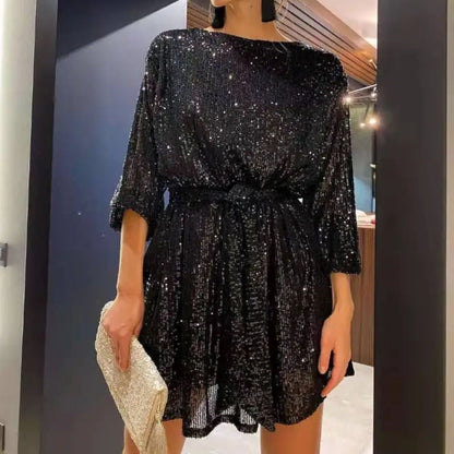 Frau in schwarzem Paillettenkleid mit goldener Clutch, elegantes Abendoutfit, Mode 2023.