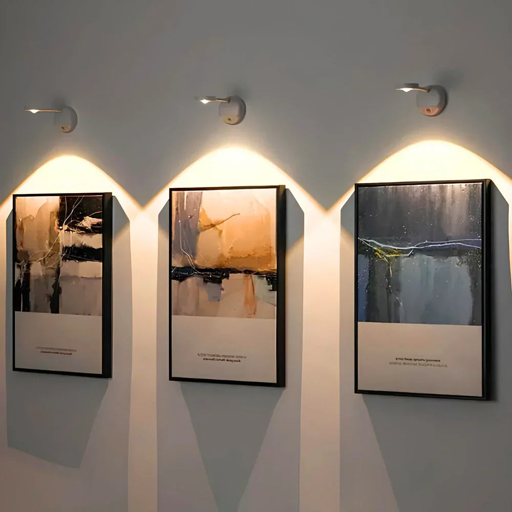 Drei moderne Wandbilder mit abstrakter Kunst, beleuchtet von LED-Wandleuchten.