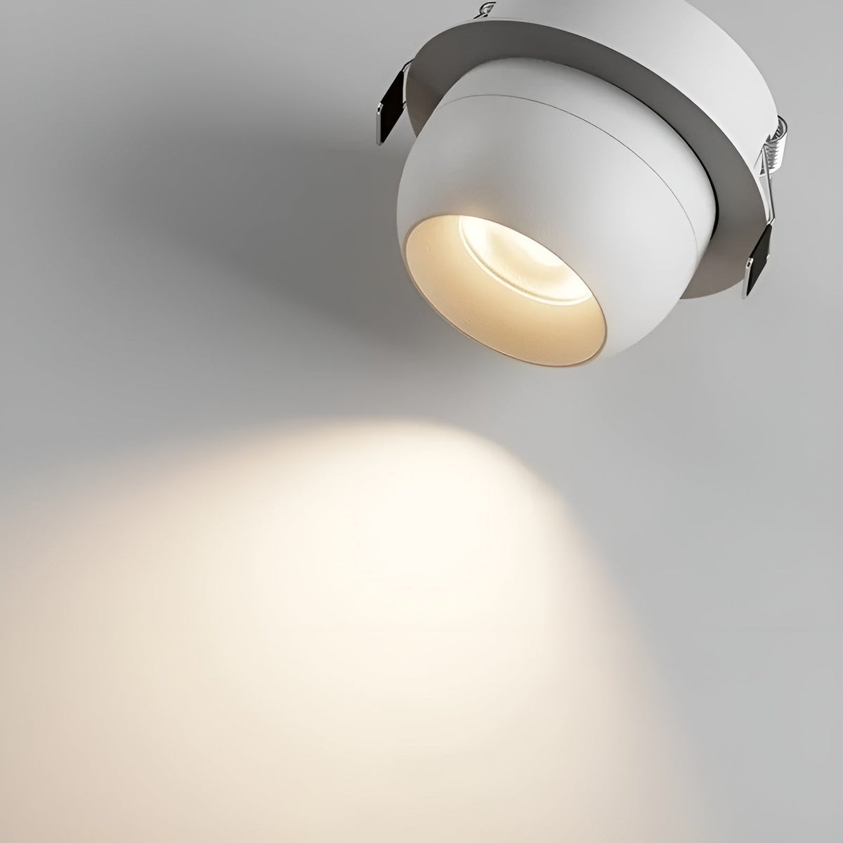 Nahaufnahme eines weißen, eingebauten Strahlers mit sichtbaren Federklammern, der einen warmen Lichtkegel auf die Fläche 4