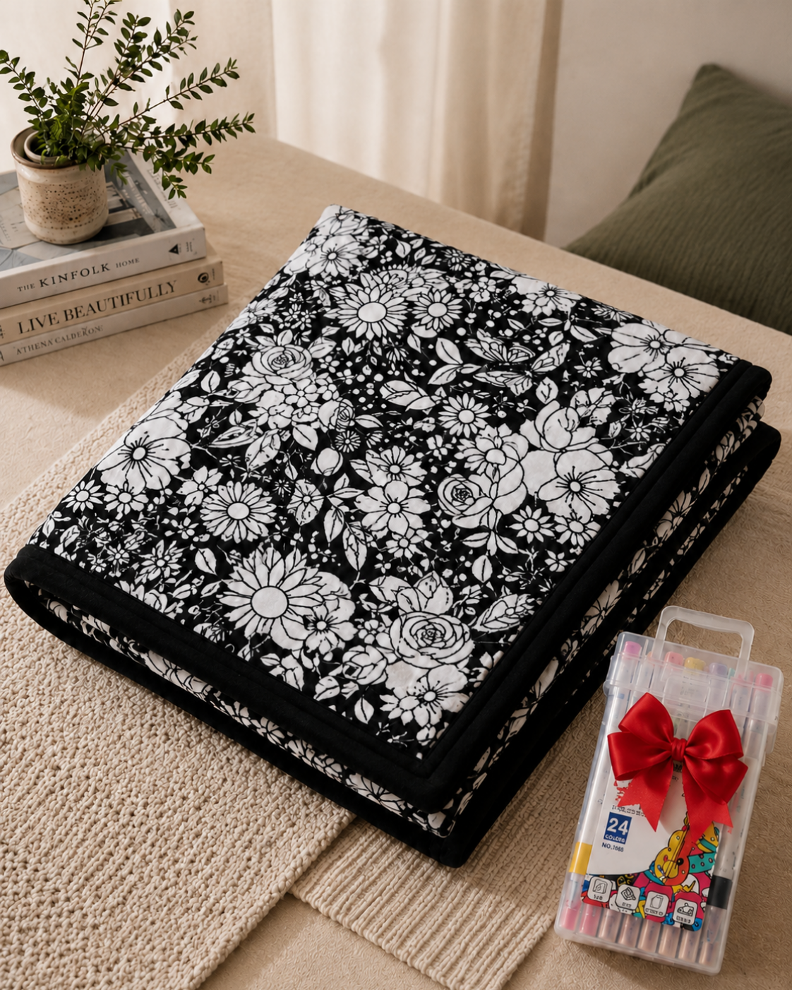 Gefaltete schwarz-weiße Decke mit Blumenmuster neben einem Stoffmarker-Set mit roter Schleife auf einem Beistelltisch 1