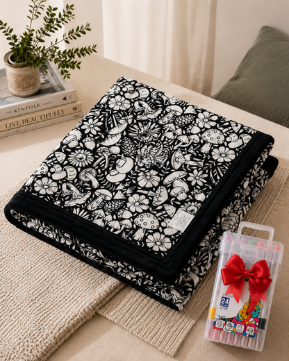 Gefaltete Decke mit Pilz- und Blumenmotiven in Weiß auf Schwarz, daneben ein Markerset mit roter Schleife 9