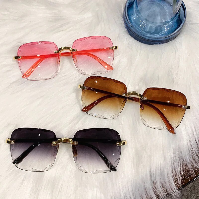 Drei Paar randlose Vintage-Sonnenbrillen auf weißem Fell, rosa, braun und schwarz.