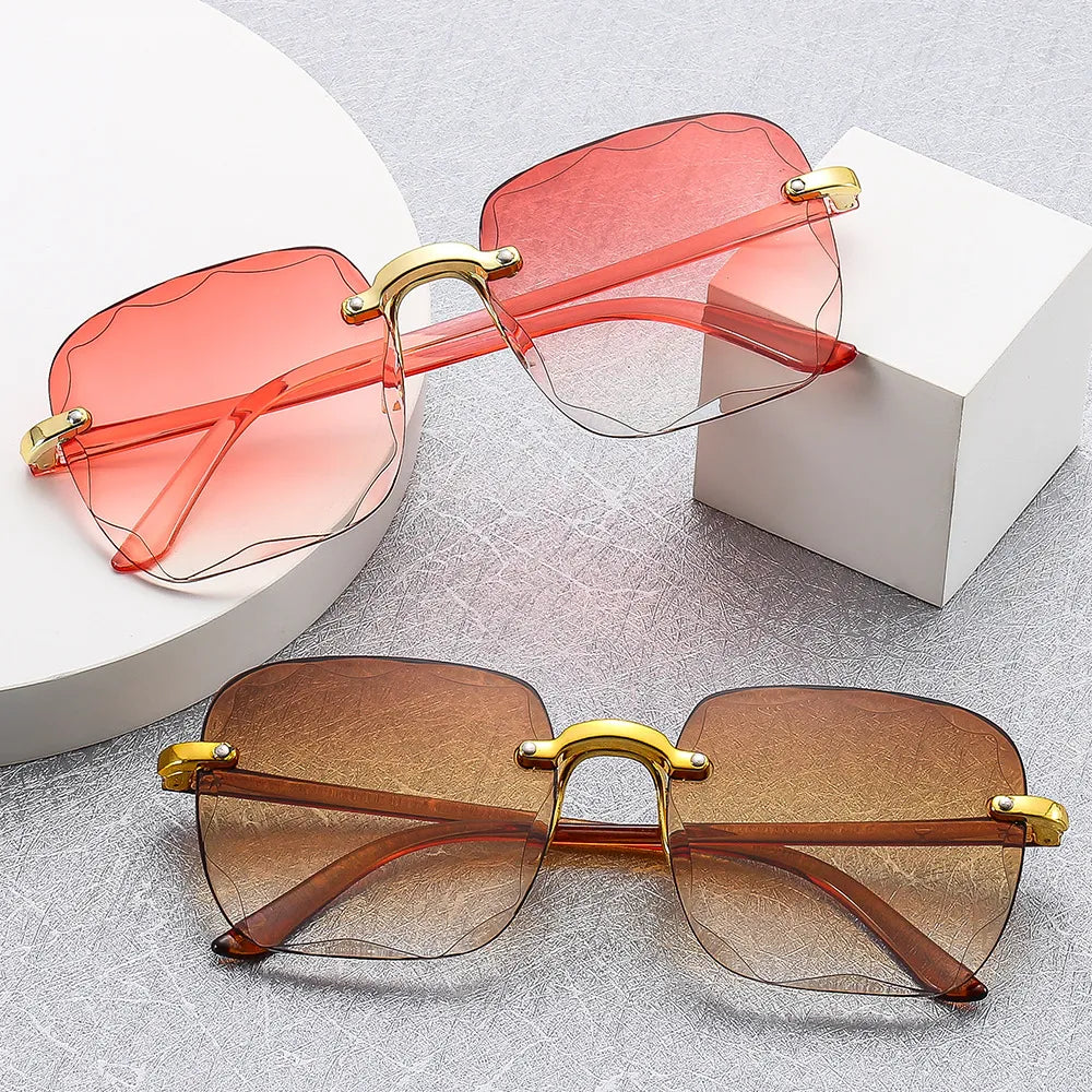 Zwei vintage randlose Sonnenbrillen, rosa und braun, mit goldenen Bügeln auf grauem Hintergrund.