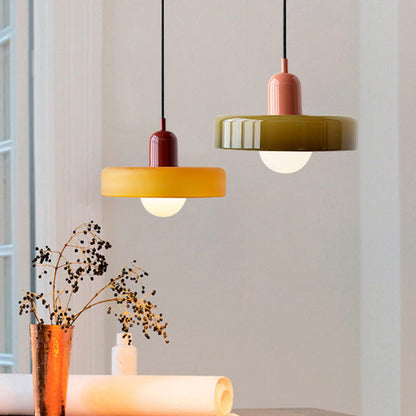 Zwei moderne Hängelampen, gelb und olivgrün, aus Glas über einem Tisch mit Dekoration.