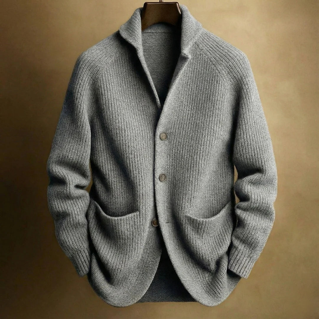 Graue Strickjacke mit grober Rippenstruktur, Raglanärmeln und zwei Taschen, am Bügel vor beigem Hintergrund 5