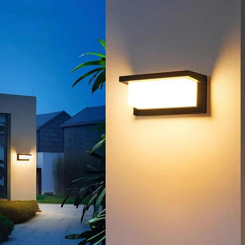 Spiegelverkehrte Ansicht der warm leuchtenden Lampe an der Hauswand, links ein Weg und Pflanzen 4