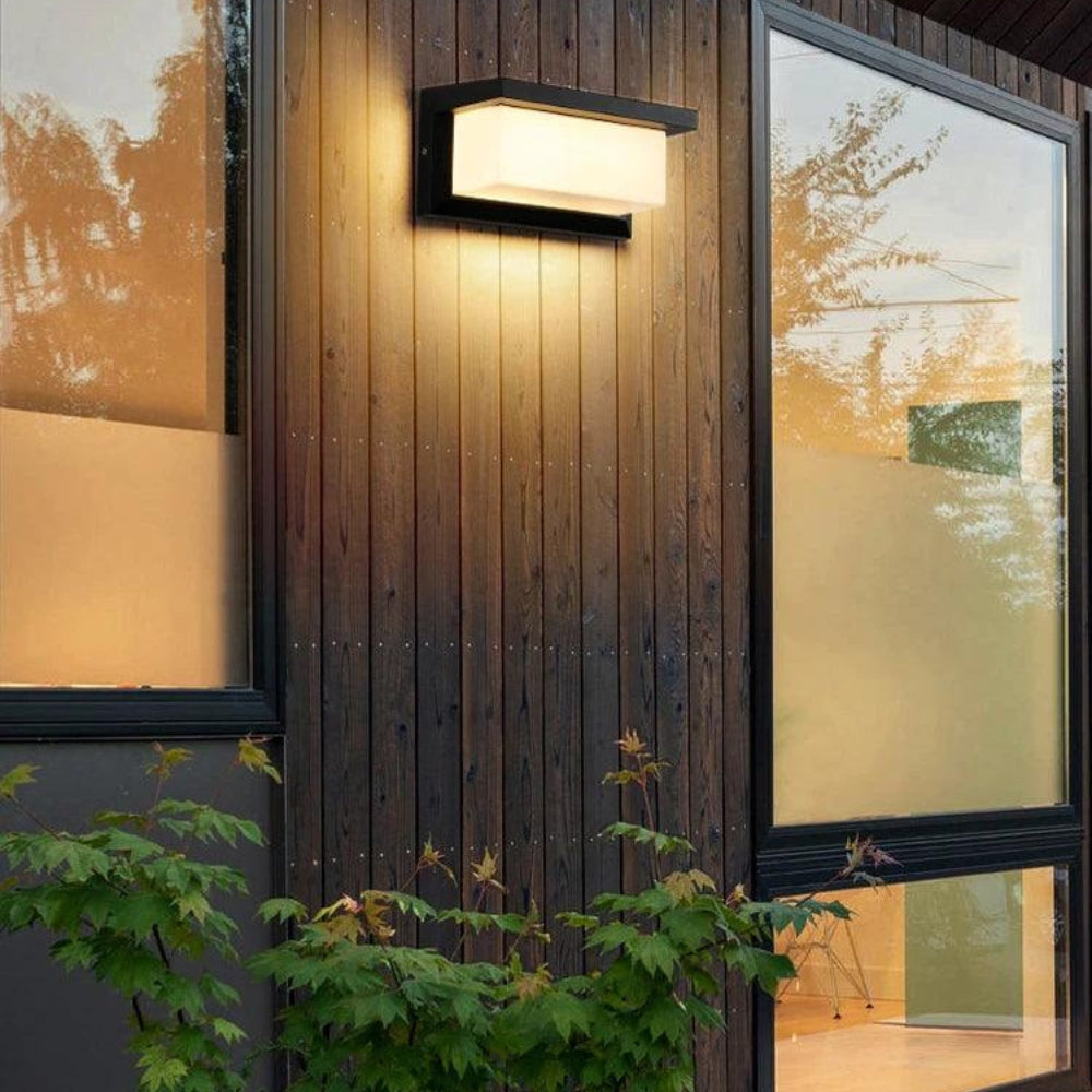 Wandlampe an dunkler Holzverkleidung zwischen zwei großen Fenstern, darunter grüne Pflanzen 5