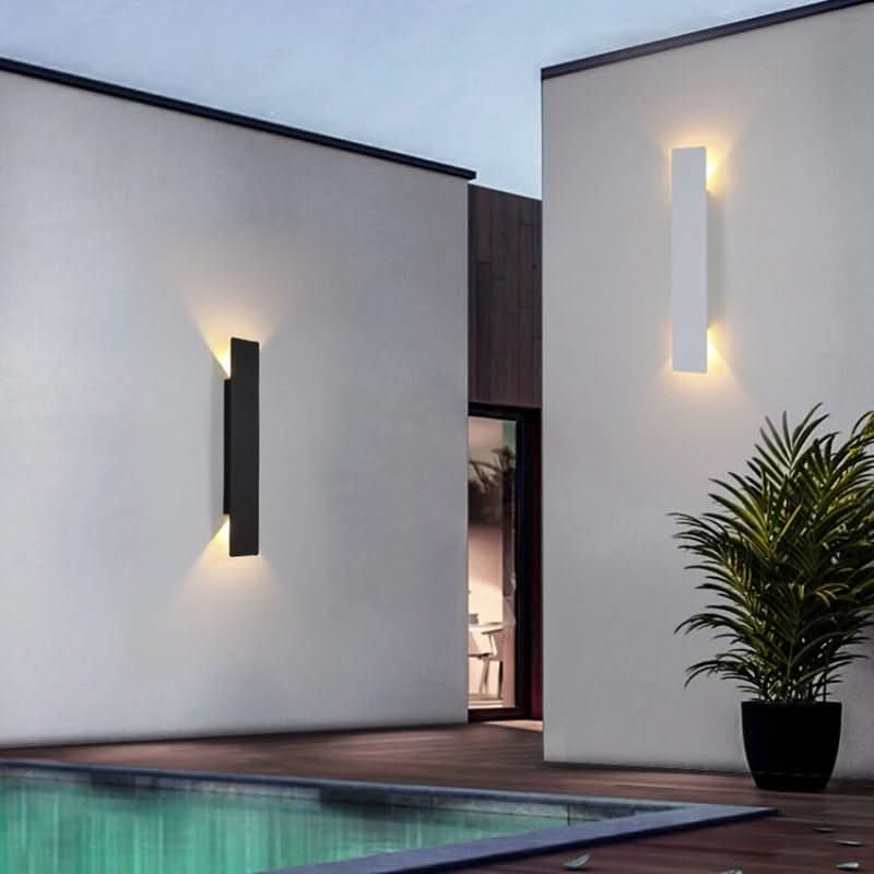 Eine schwarze und eine weiße Wandleuchte an weißen Hauswänden neben einem Pool, mit Topfpflanze im Vordergrund und warmem Auf-und-ab-Licht. 4