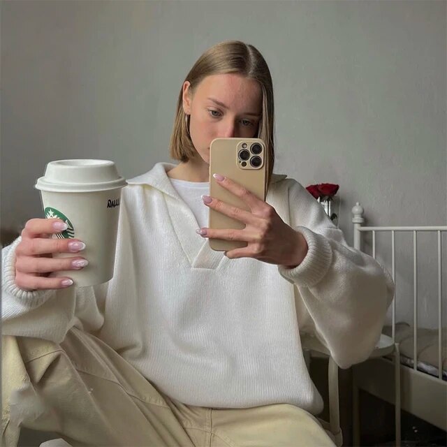 Frau in weißem Pullover mit Smartphone und Starbucks-Becher, Selfie im Schlafzimmer.