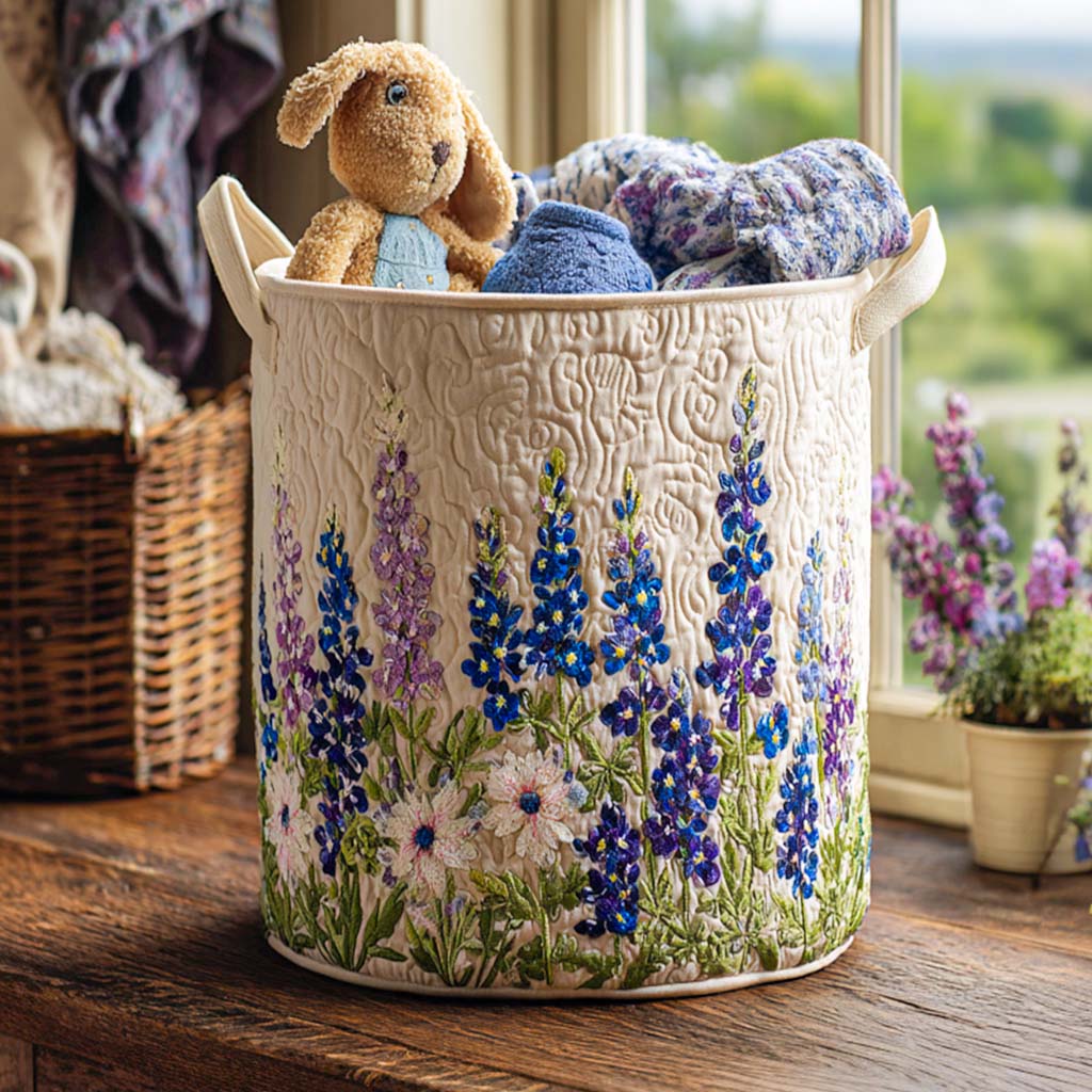 Cremefarbener gesteppter Korb mit gestickten blauen und lila Blumen auf einem Holzbrett am Fenster, gefüllt mit Plüschhase und Textilien. 1