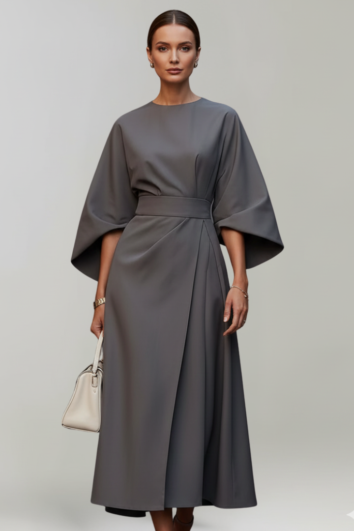 Model im grauen Kleid mit weiten Ärmeln, Taillengürtel und leicht ausgestelltem Wickelrock, dazu eine cremefarbene 10