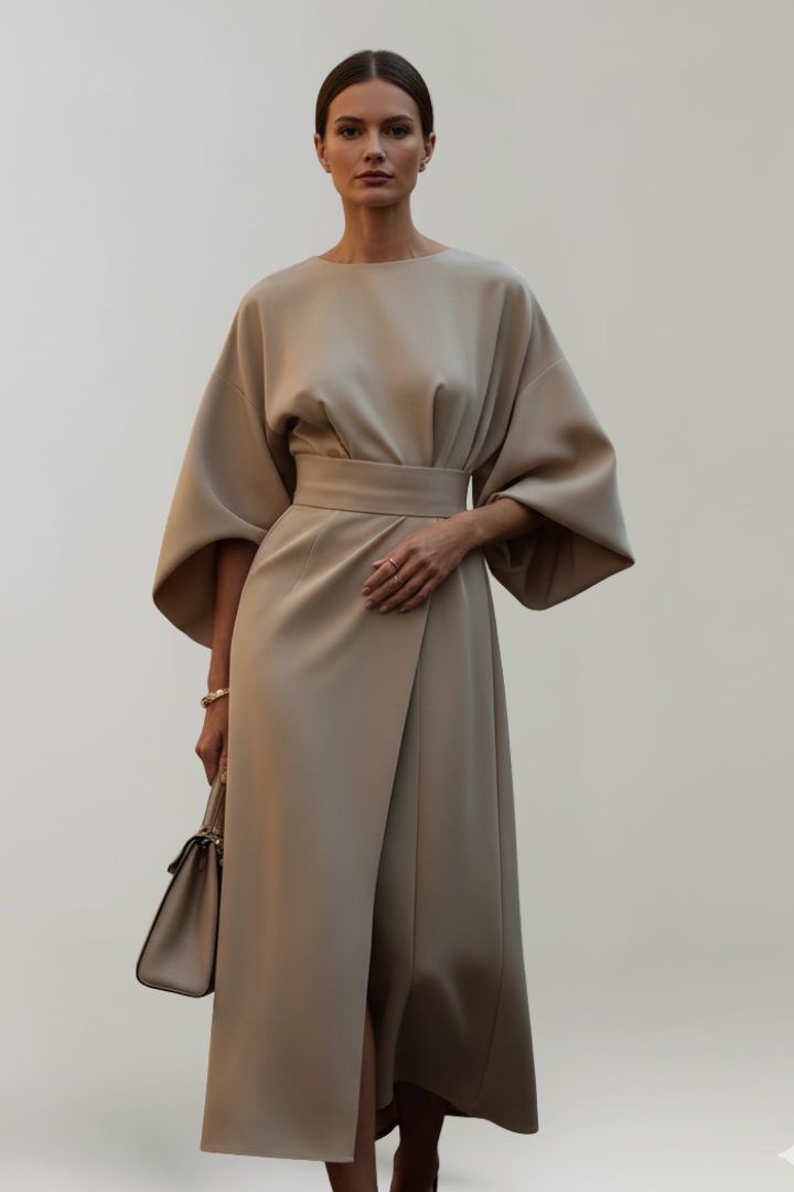 Model im beigefarbenen Kleid mit weiten Ärmeln, Taillengürtel und seitlichem Wickelrock, dazu eine helle Handtasche 6