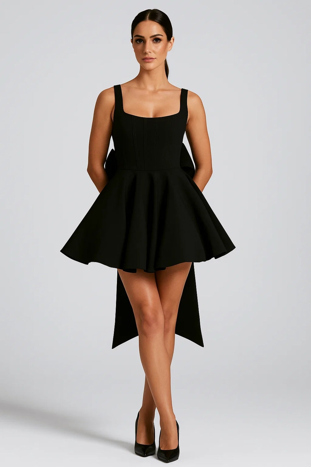 Model trägt das Minikleid in Schwarz mit gerippter Bustier-Optik, Schleife am Rücken und schwarzen Pumps 8
