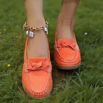 Orangefarbene Loafer mit geflochtener Zierbrücke, getragen im Gras mit goldenem Fußkettchen mit Perlenanhängern, Frontansicht. 4