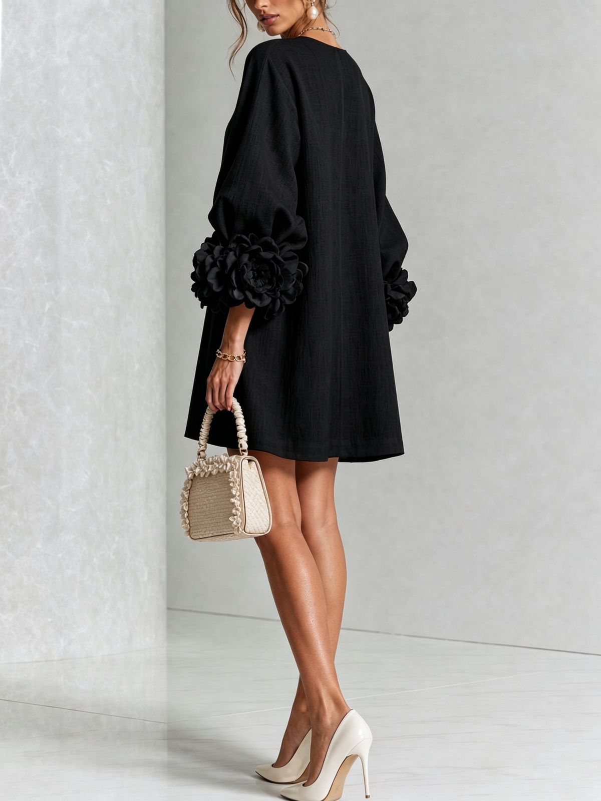 Schwarzes Minikleid von hinten mit Rosenmanschetten an beiden Ärmeln, Model hält eine Handtasche. 17