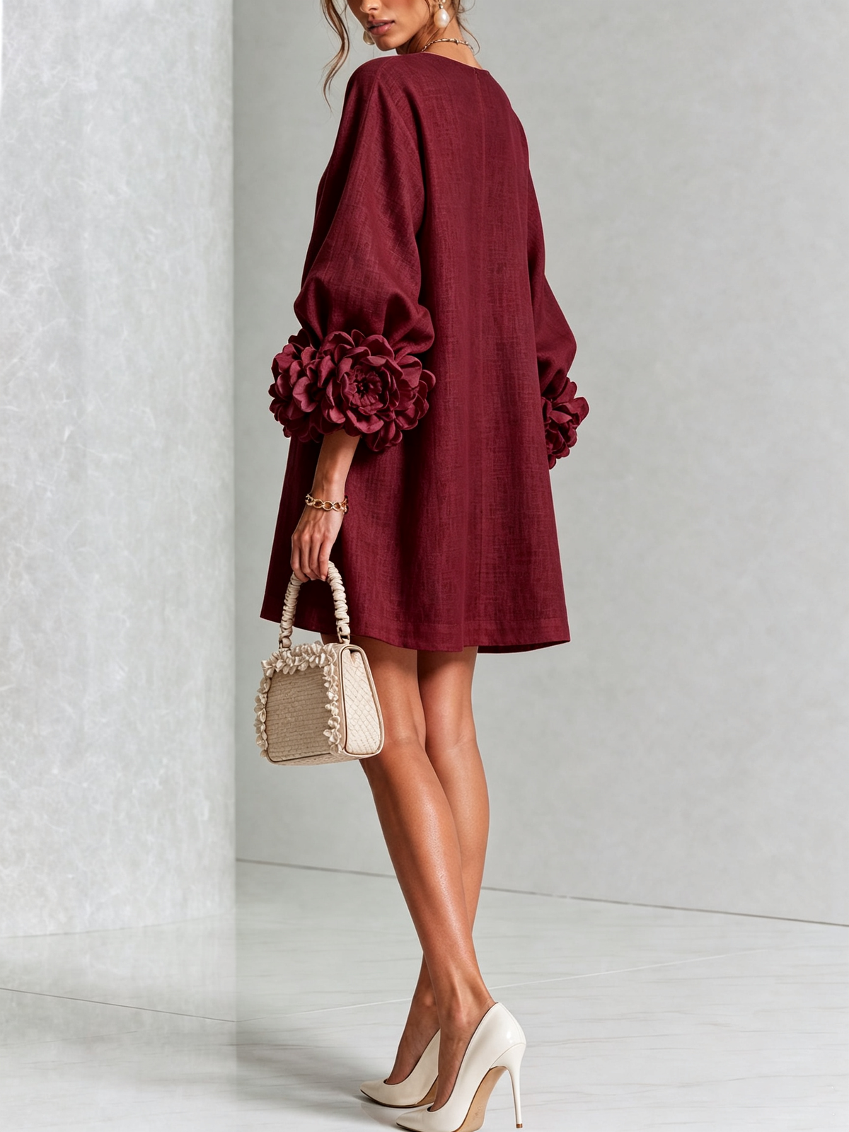 Weinrotes Kleid von hinten gezeigt mit glattem Rücken und großer Rosenmanschette am Ärmel, dazu helle Handtasche und Pumps. 37
