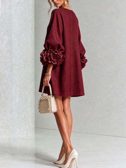 Weinrotes Kleid von hinten gezeigt mit glattem Rücken und großer Rosenmanschette am Ärmel, dazu helle Handtasche und Pumps. 37