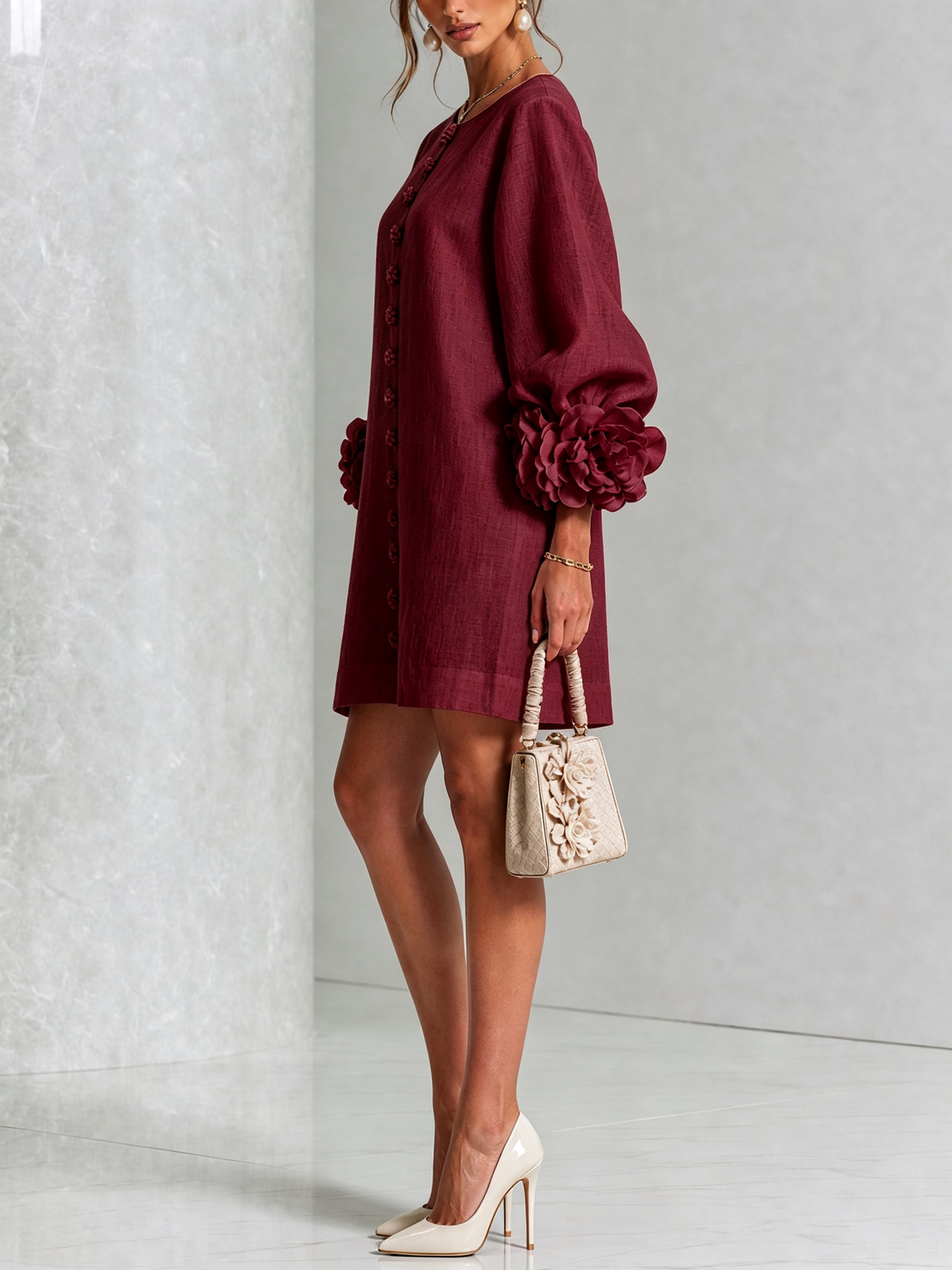Weinrotes Kleid in der Seitenansicht mit Blütenknöpfen und Rosenmanschette am Puffärmel, dazu helle Handtasche mit Blüten und Pumps. 36