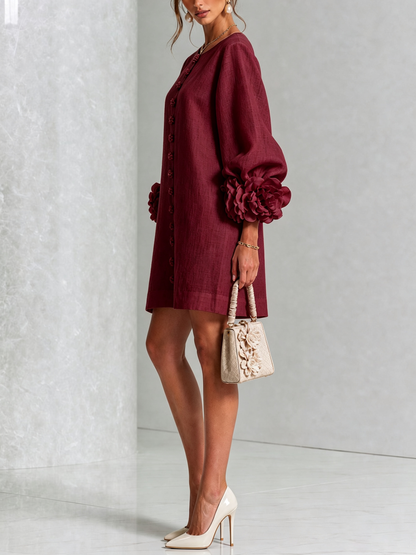Weinrotes Kleid in der Seitenansicht mit Blütenknöpfen und Rosenmanschette am Puffärmel, dazu helle Handtasche mit Blüten und Pumps. 36