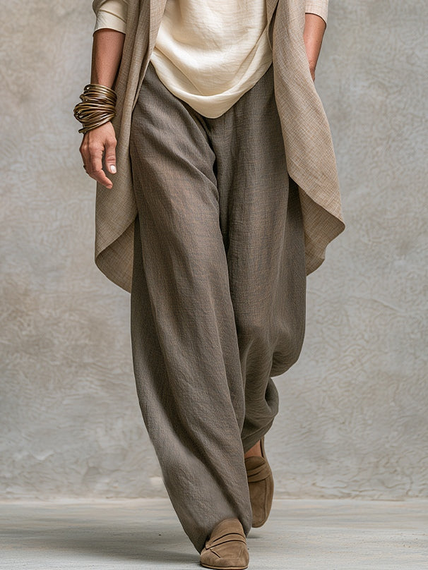Detailansicht der weiten graubraunen Hose mit lockerem Fall, dazu Jackett-Saum, Oberteil-Saum und Wildleder-Slipper. 5