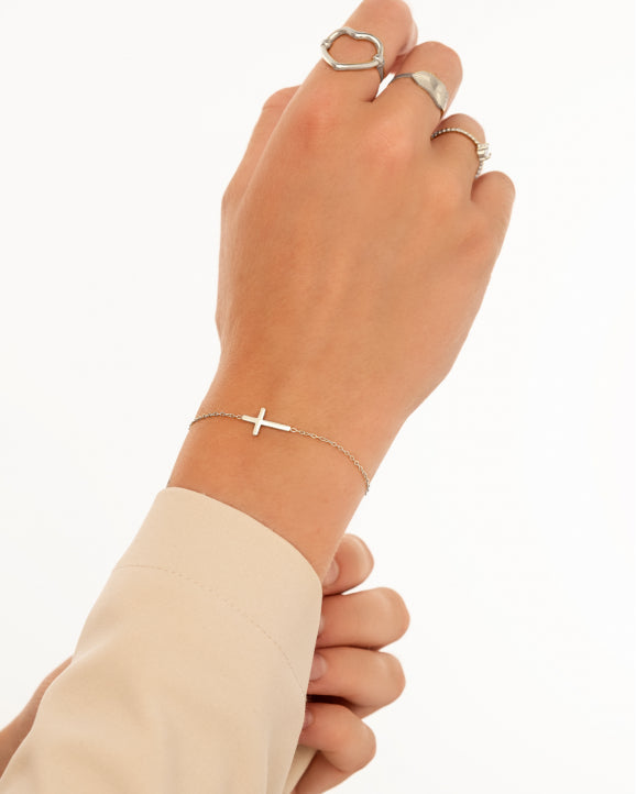 Silbernes Kreuzarmband an Handgelenk, elegantes Schmuckstück, minimalistisch, Damenmode.