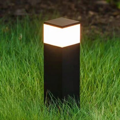 Nahaufnahme einer schwarzen rechteckigen Pollerleuchte mit hell leuchtendem warmweißem Lichtband, im Gras stehend. 7
