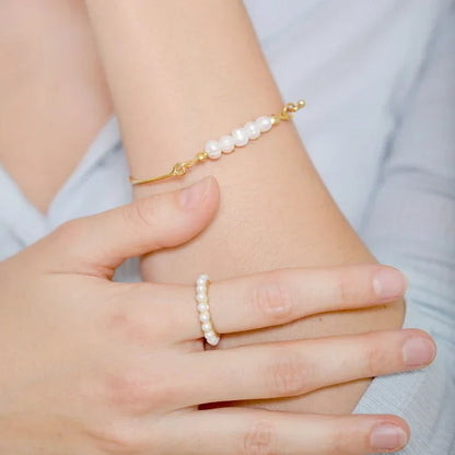 Goldenes Armband und Ring mit weißen Perlen auf Handgelenk, eleganter Schmuck für Damen.