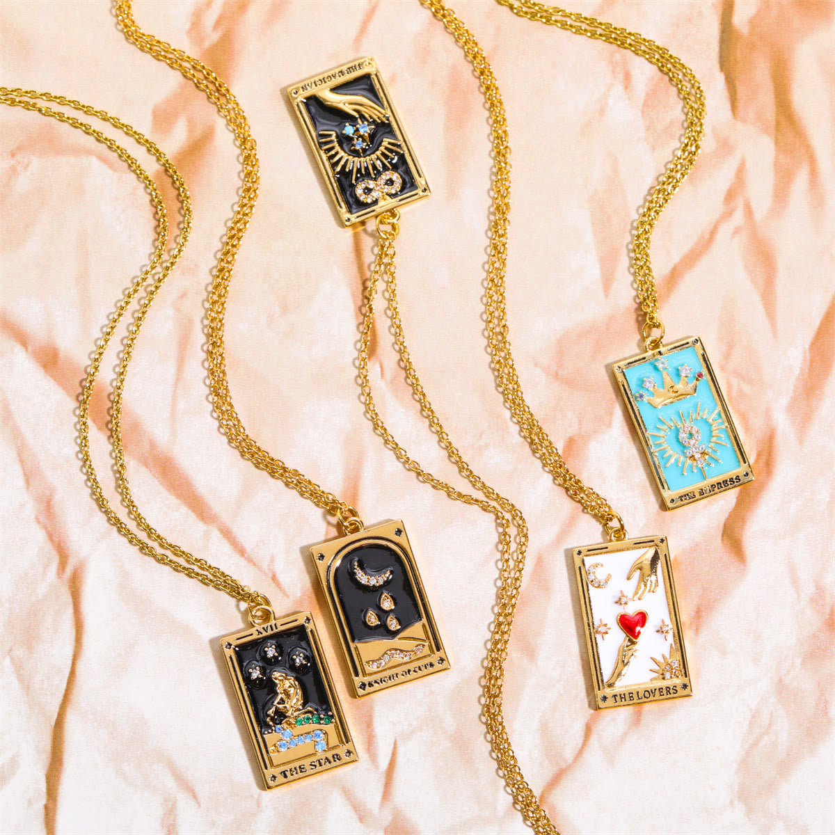 Fünf goldene Tarot-Anhänger mit Ketten auf beigem Hintergrund, Schmuck, Esoterik, Geschenkideen.