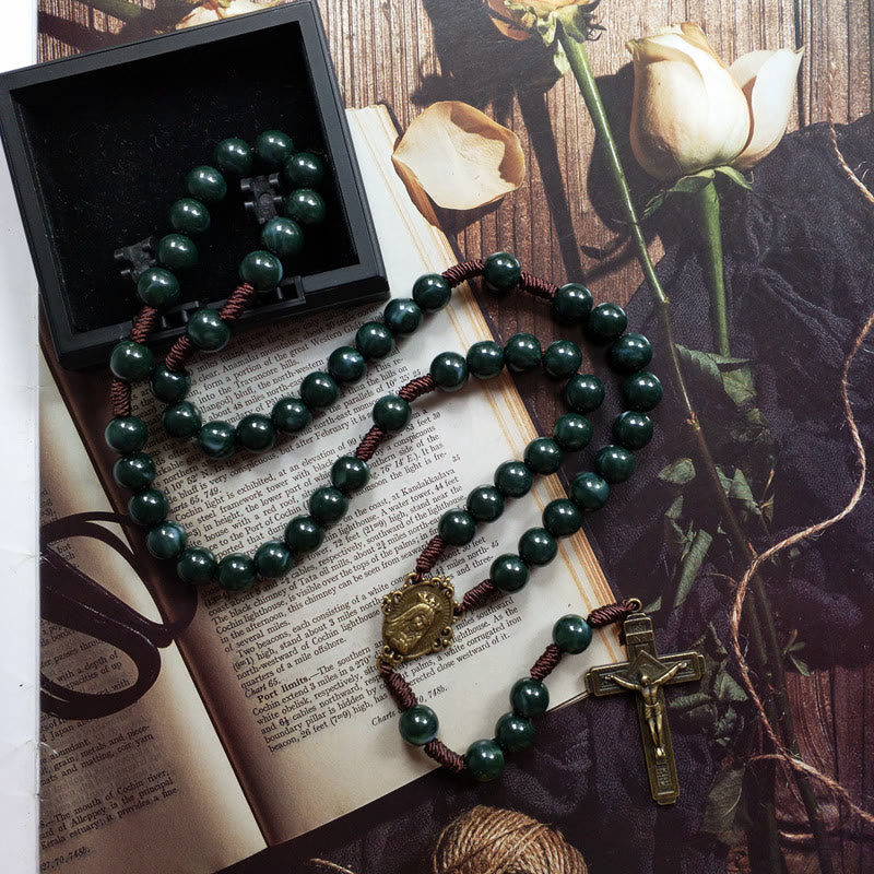 Dunkelgrüner Rosenkranz mit Kreuz und Medaillon auf offenem Buch, religiöses Schmuckstück.