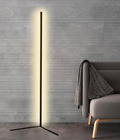 Freistehende schwarze Stehleuchte mit warmweißem Licht vor einer grauen Wand, daneben ein Sessel mit Decke 8