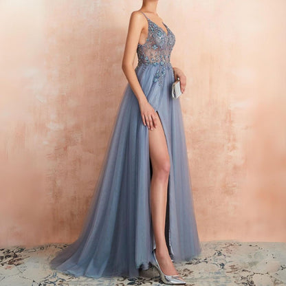 Frau in langem, blauem Abendkleid mit Spitze und hohem Schlitz, hält silberne Clutch.