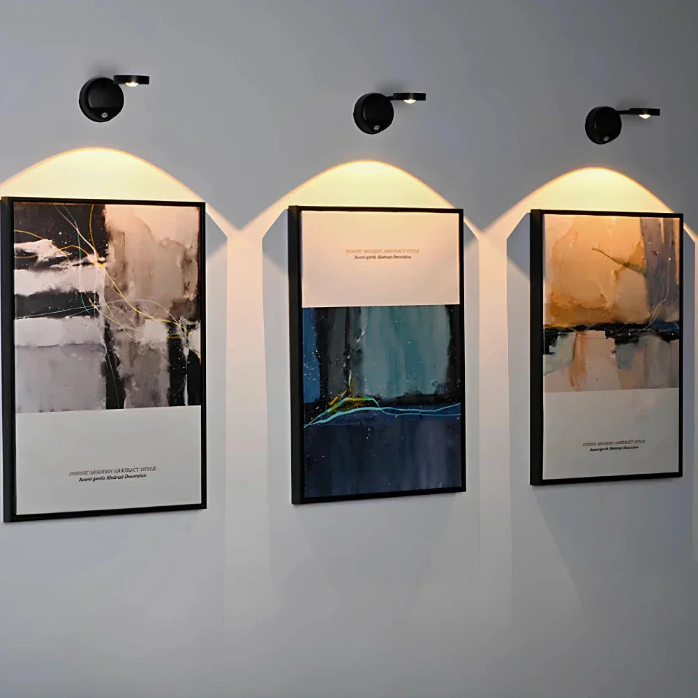 Drei moderne abstrakte Gemälde mit schwarzem Rahmen, beleuchtet an einer grauen Wand.