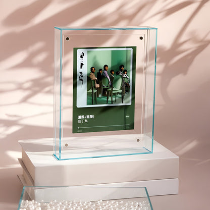 Klarer Acrylrahmen mit grünlicher Kante steht auf weißen Büchern und zeigt ein Gruppenfoto in Grüntönen, im Hintergrund Schattenspiel. 13
