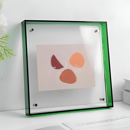 Quadratischer Acrylrahmen mit grüner Kante und silbernen Eckhaltern steht auf einem Tisch und zeigt eine abstrakte Kunstkarte. 21