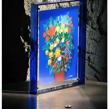 Blauer Acrylrahmen mit Blumenstrauß-Druck steht auf einer Fläche vor einer rauen Steinwand. 4