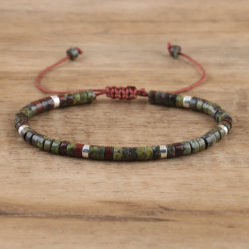 Armband aus grünen und braunen Steinen, verstellbar, handgefertigt, auf Holzoberfläche.