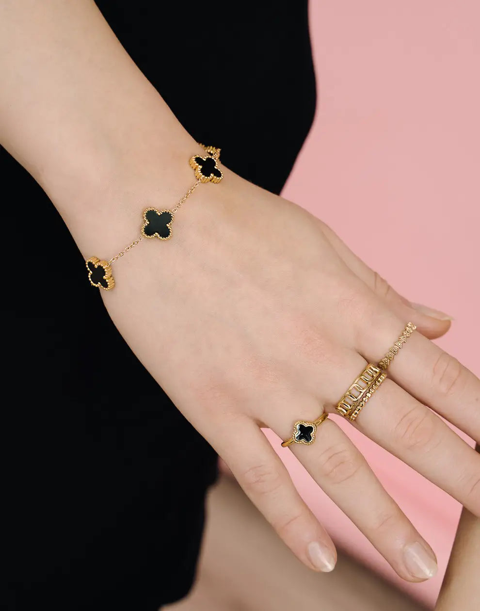 Goldenes Armband mit schwarzen Kleeblatt-Anhängern auf Hand, eleganter Schmuck, Damenaccessoire.