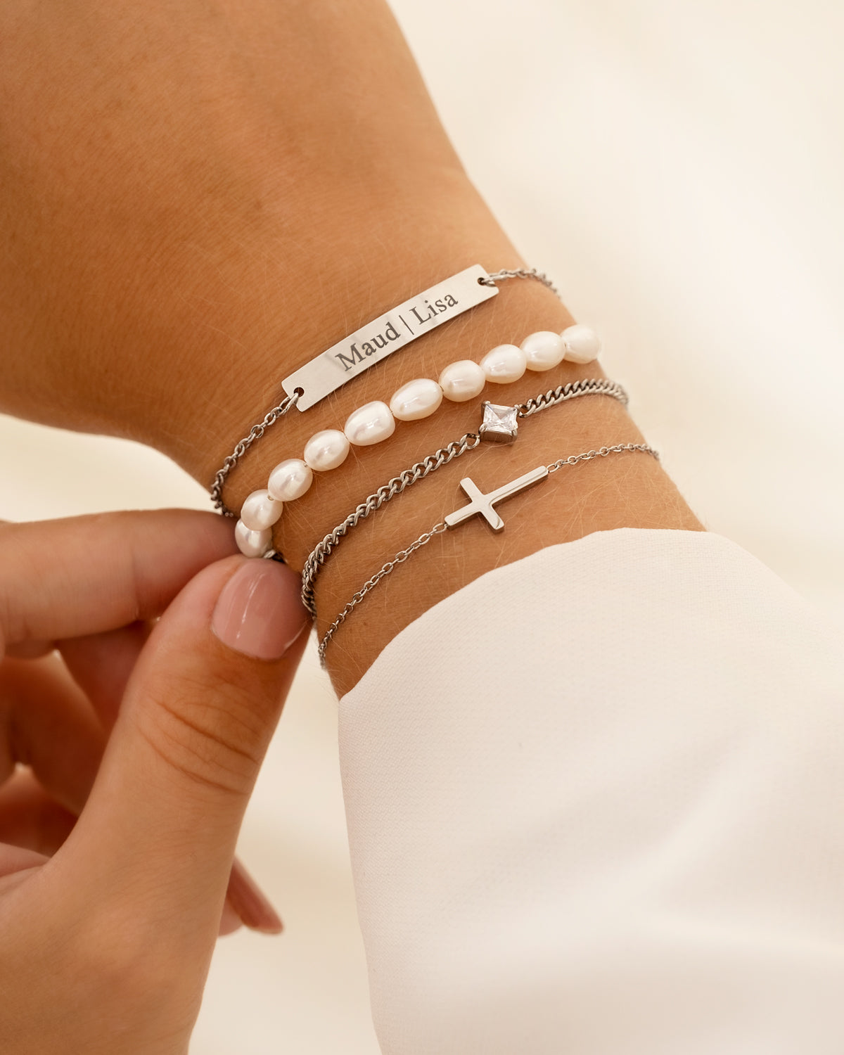 Silberne Armbänder mit Perlen und Kreuzanhänger auf Handgelenk, modisches Schmuckdesign.