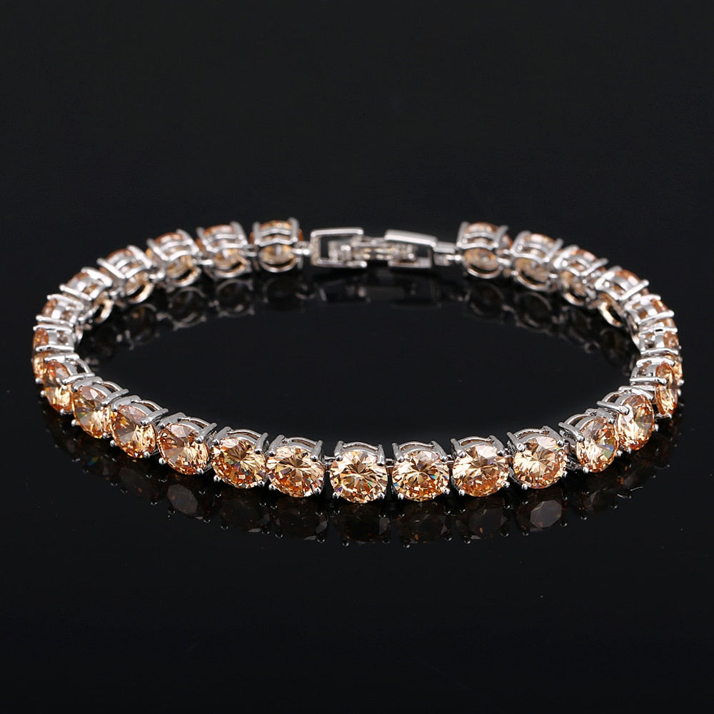 Silbernes Tennisarmband mit runden, champagnerfarbenen Zirkonia-Steinen auf schwarzem Hintergrund.