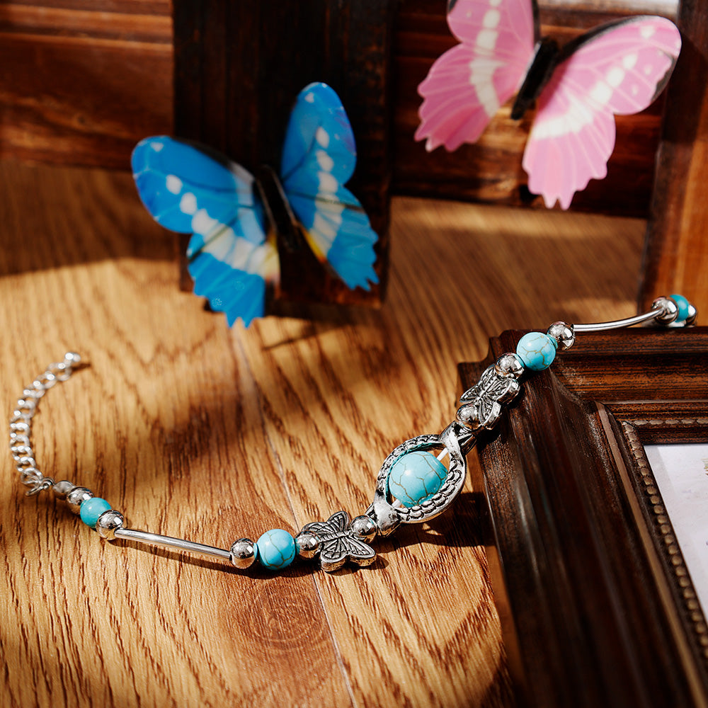 Silberarmband mit blauen Perlen und Schmetterlingsanhänger auf Holztisch, Schmuck für Damen.