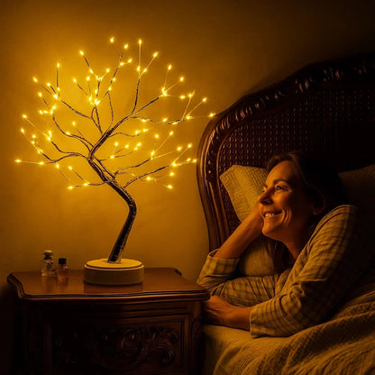 Leuchtender Lichterbaum auf einem Holz-Nachttisch, daneben eine lächelnde Frau im Bett im warmen Schein 1