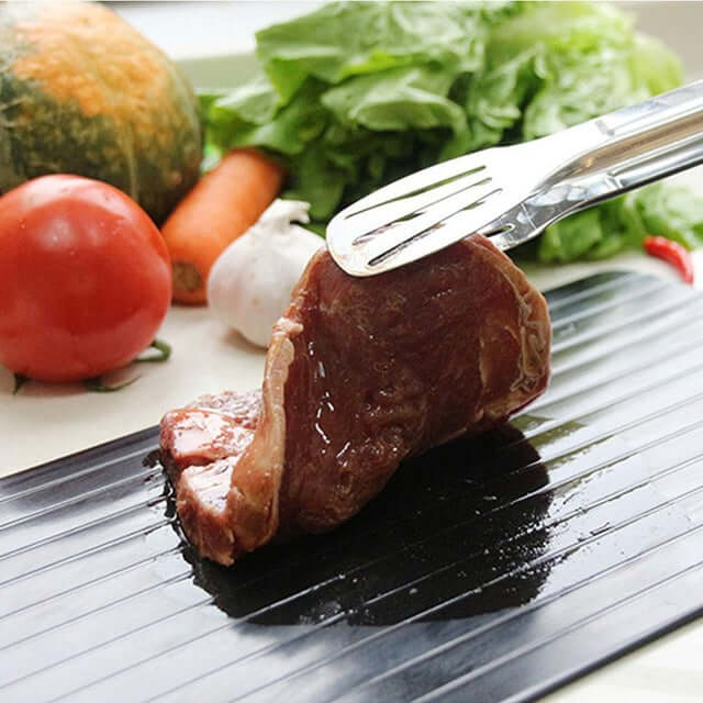Schnellauftau-Tablett mit gefrorenem Fleisch, Gemüse im Hintergrund, schwarz, Aluminium.