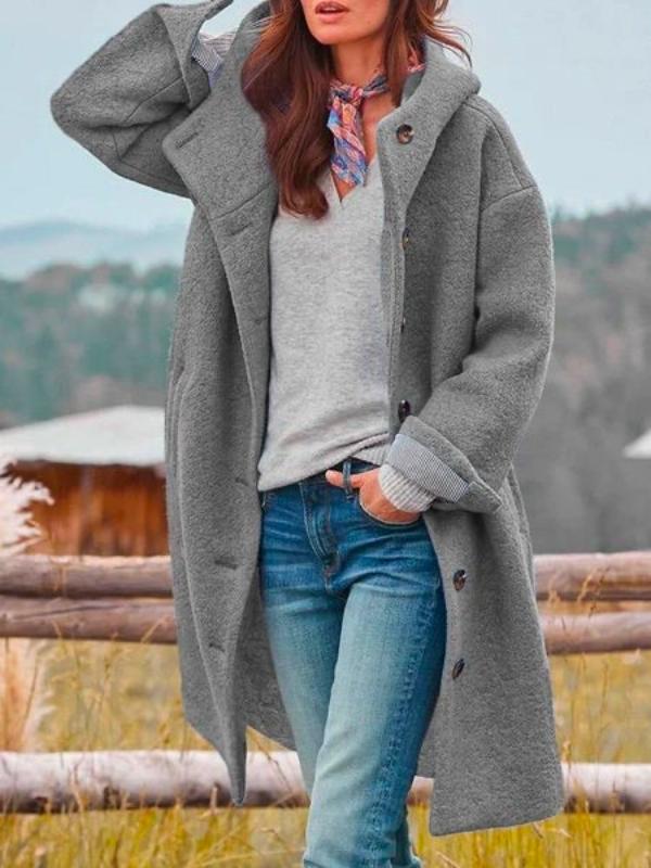 Mantel in Grau mit Kapuze und Knöpfen, getragen über grauem Pullover, Halstuch und Jeans, ein Arm locker erhoben. 2