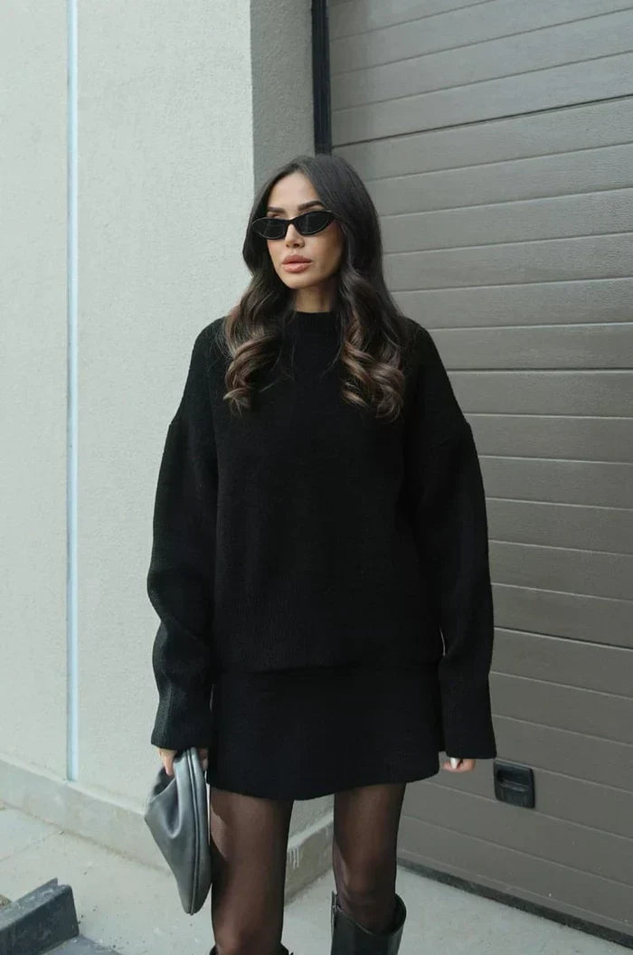 Model in schwarzem Strick-Zweiteiler mit langem, weitem Pullover und kurzem Rock, dazu Strumpfhose und schwarze Stiefel. 5