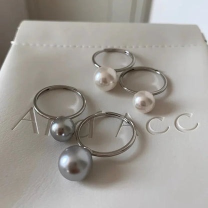 Silberne Ringe mit weißen und grauen Perlen auf weißem Hintergrund, eleganter Schmuck.