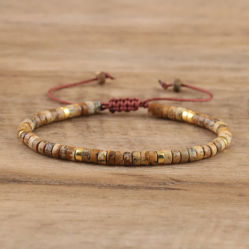 Armband aus Natursteinperlen, braun und gold, verstellbar, handgefertigt, auf Holzoberfläche.
