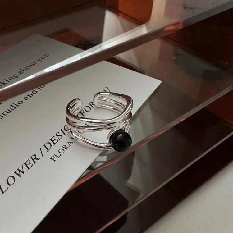 Silberner offener Ring mit schwarzem Stein auf transparentem Regal, modernes Schmuckdesign.
